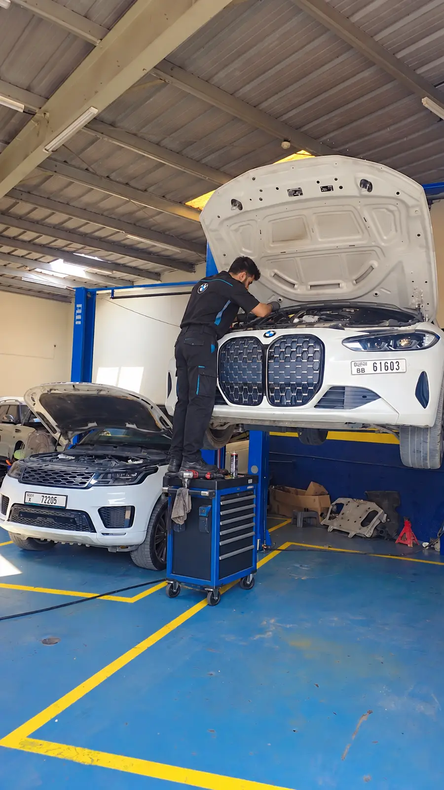 فني يقف على عربة أدوات ويعمل على محرك BMW بيضاء مرفوعة على رافعة