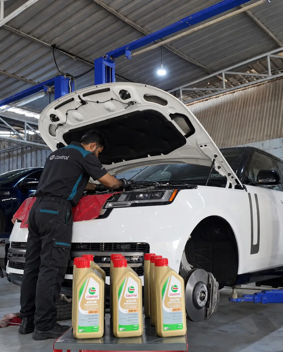 فني يعمل على محرك رنج روفر بيضاء وأمامها عبوات زيت محرك جديدة